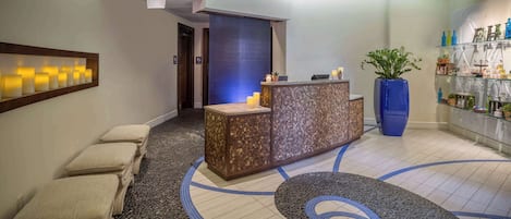 A reception area with a reception desk, a seating area with cushioned benches, a decorative floor pattern, and a potted plant.