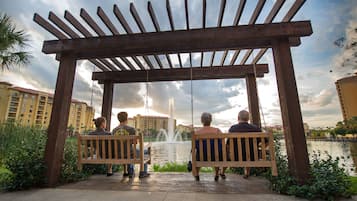 A wooden pergola with swings overlooking a body of water with buildings in the background.