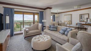 A spacious living room with a large window, a sofa set, a coffee table, and a television. - Wyndham Grand Orlando Resort Bonnet Creek (Orlando)