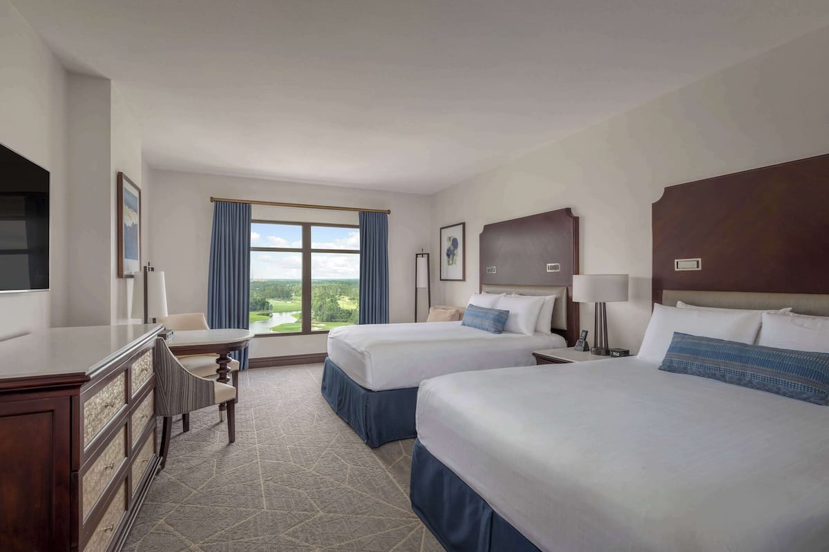 Een hotelkamer met twee bedden, een bureau, een stoel en een groot raam met uitzicht op de omgeving.