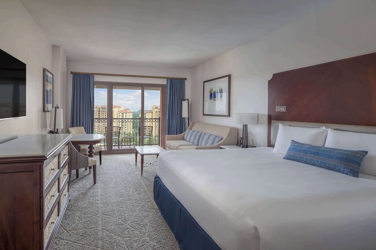 Een hotelkamer met een groot bed, een bureau, een stoel, een klein tafeltje en een balkon met uitzicht over de stad.