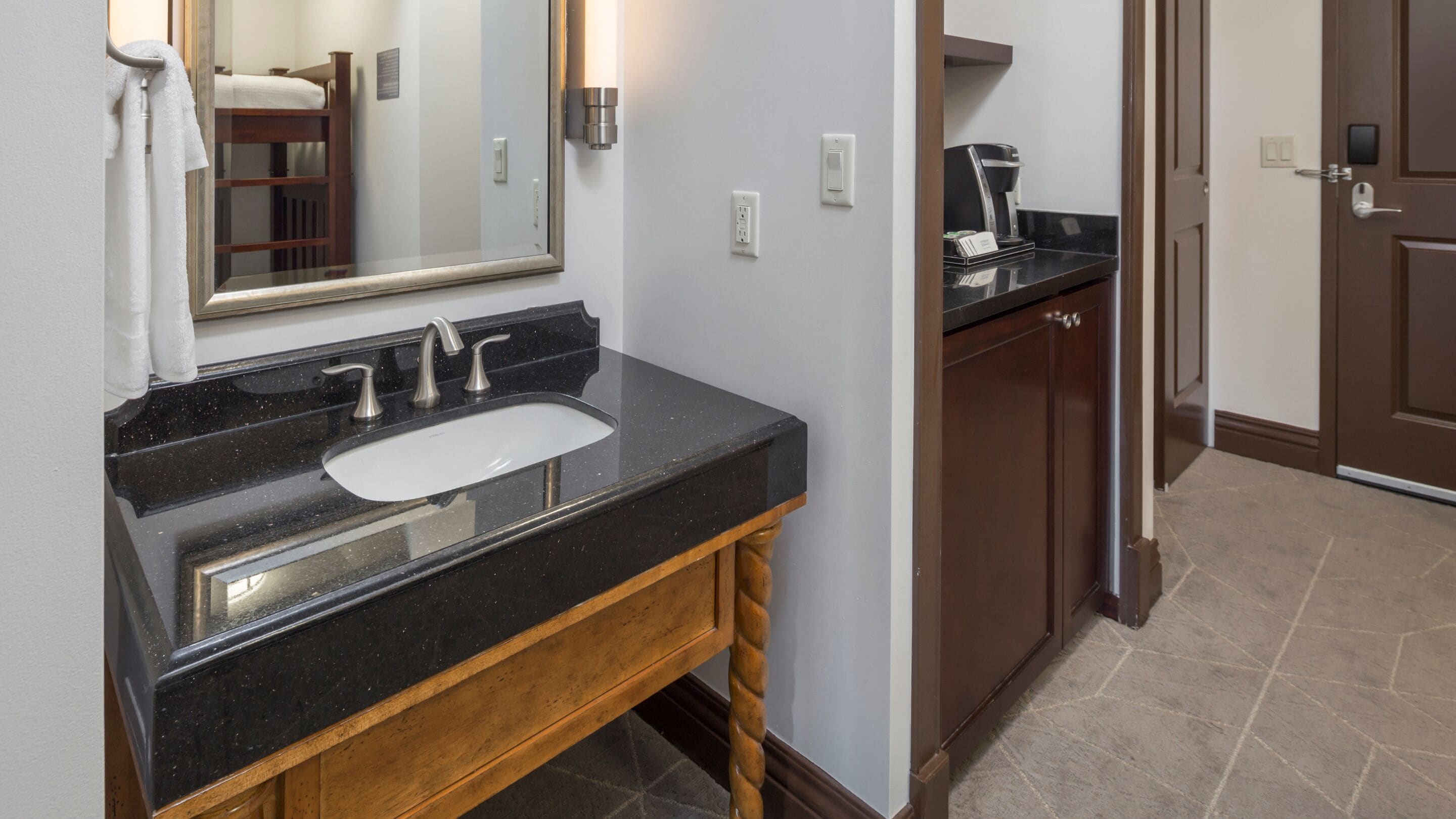 A bathroom with a black countertop sink, a wooden vanity, a mirror, and a coffee machine.