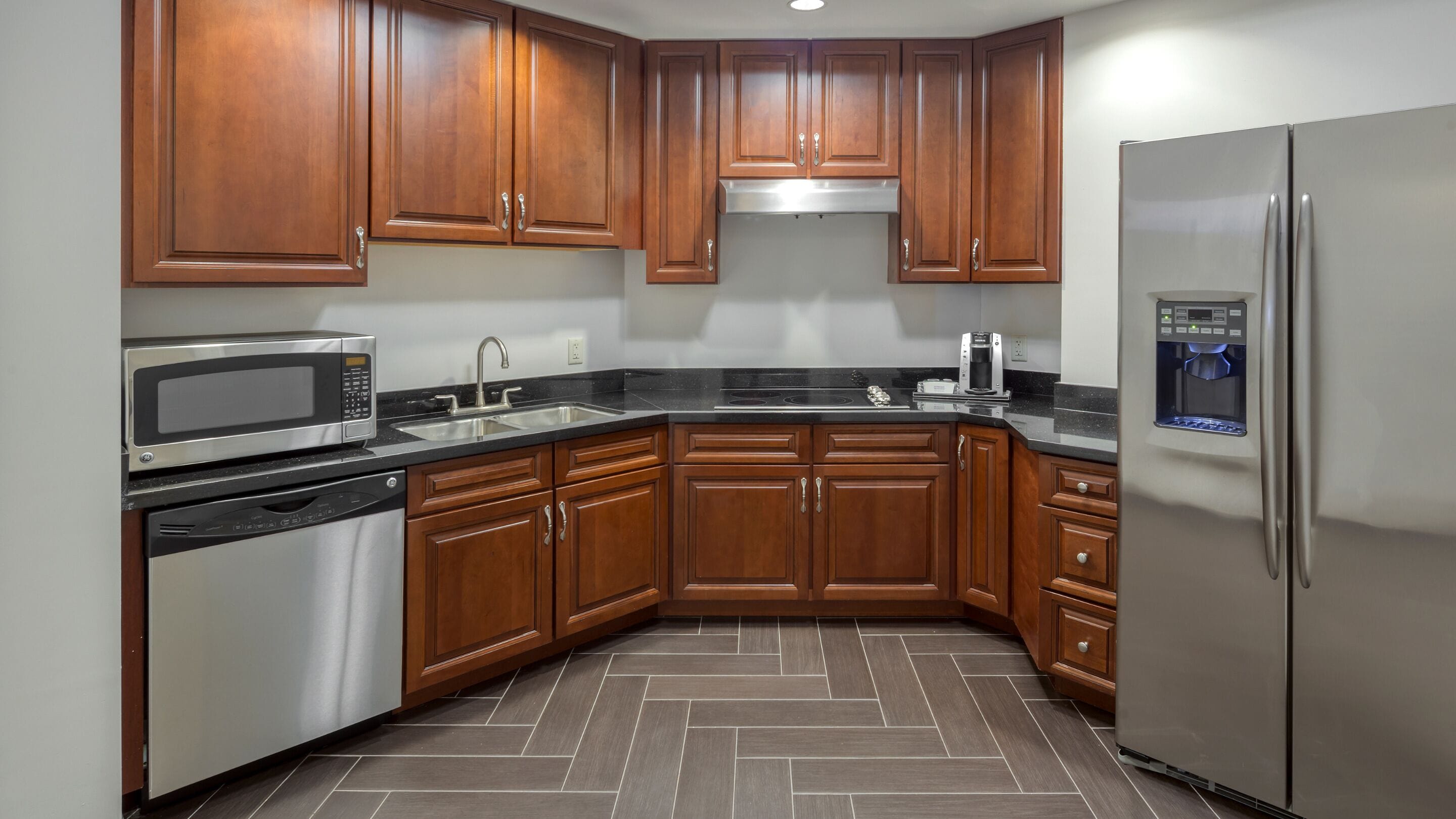 A modern kitchen with wooden cabinets, stainless steel appliances, and a herringbone tile floor.