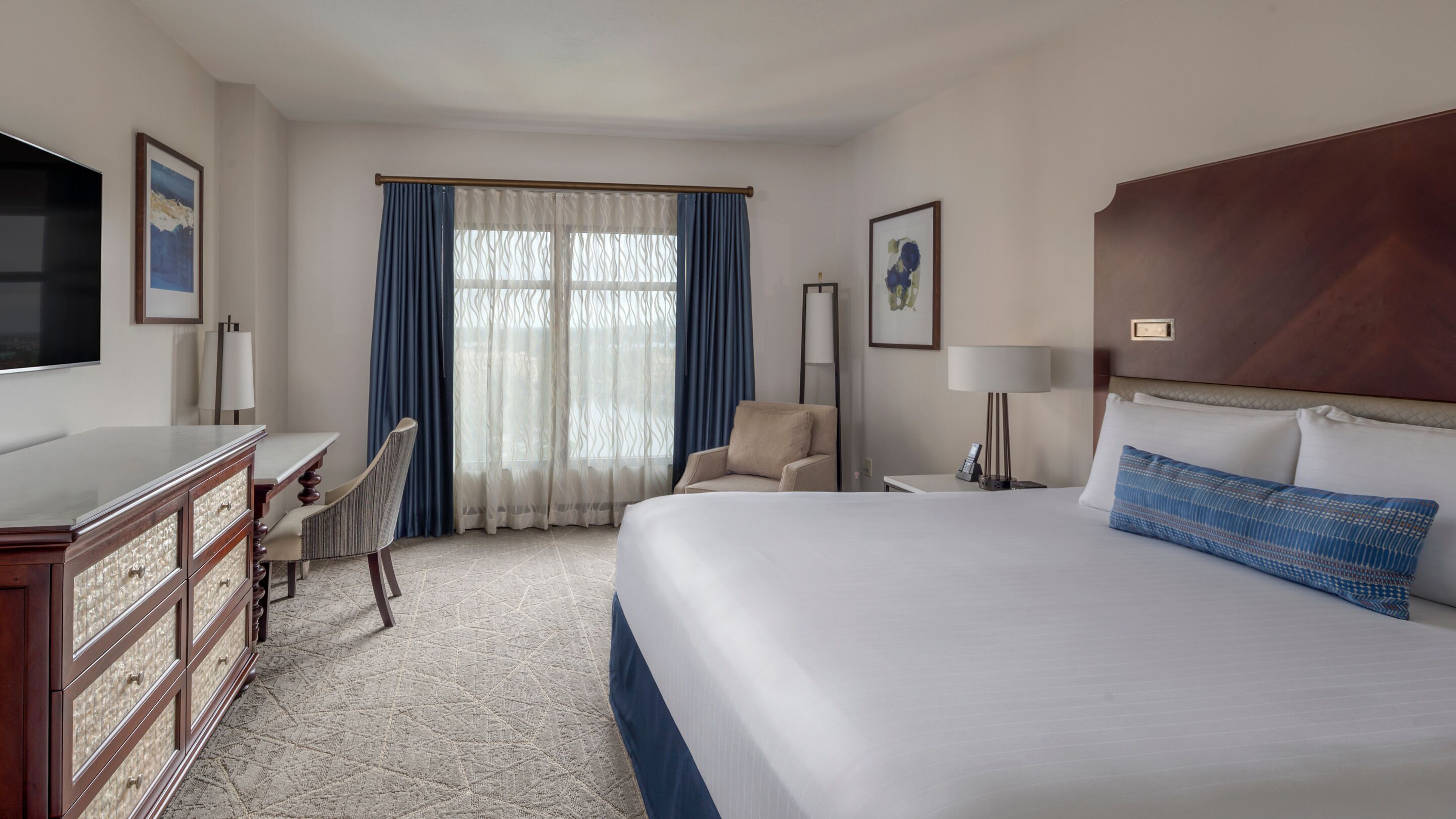 A hotel room with a large bed, a desk with a chair, a TV, and a window with curtains.