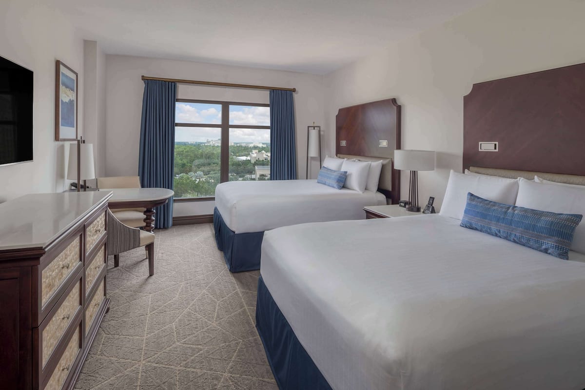 Een hotelkamer met twee bedden, een bureau, een dressoir en een groot raam met uitzicht.