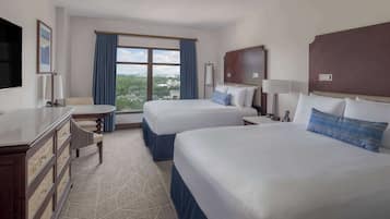 A hotel room with two beds, a desk, a dresser, and a large window offering a view.