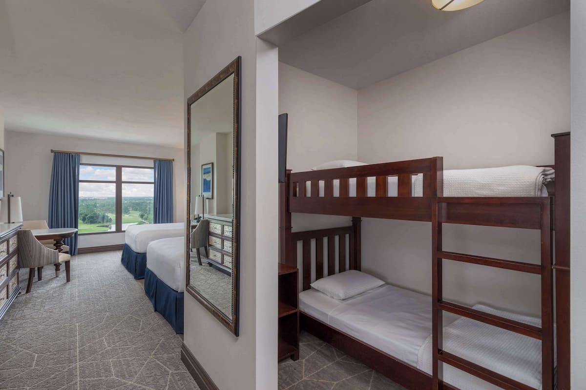 Een hotelkamer met een bureau, twee bedden, een spiegel en uitzicht op de omgeving.