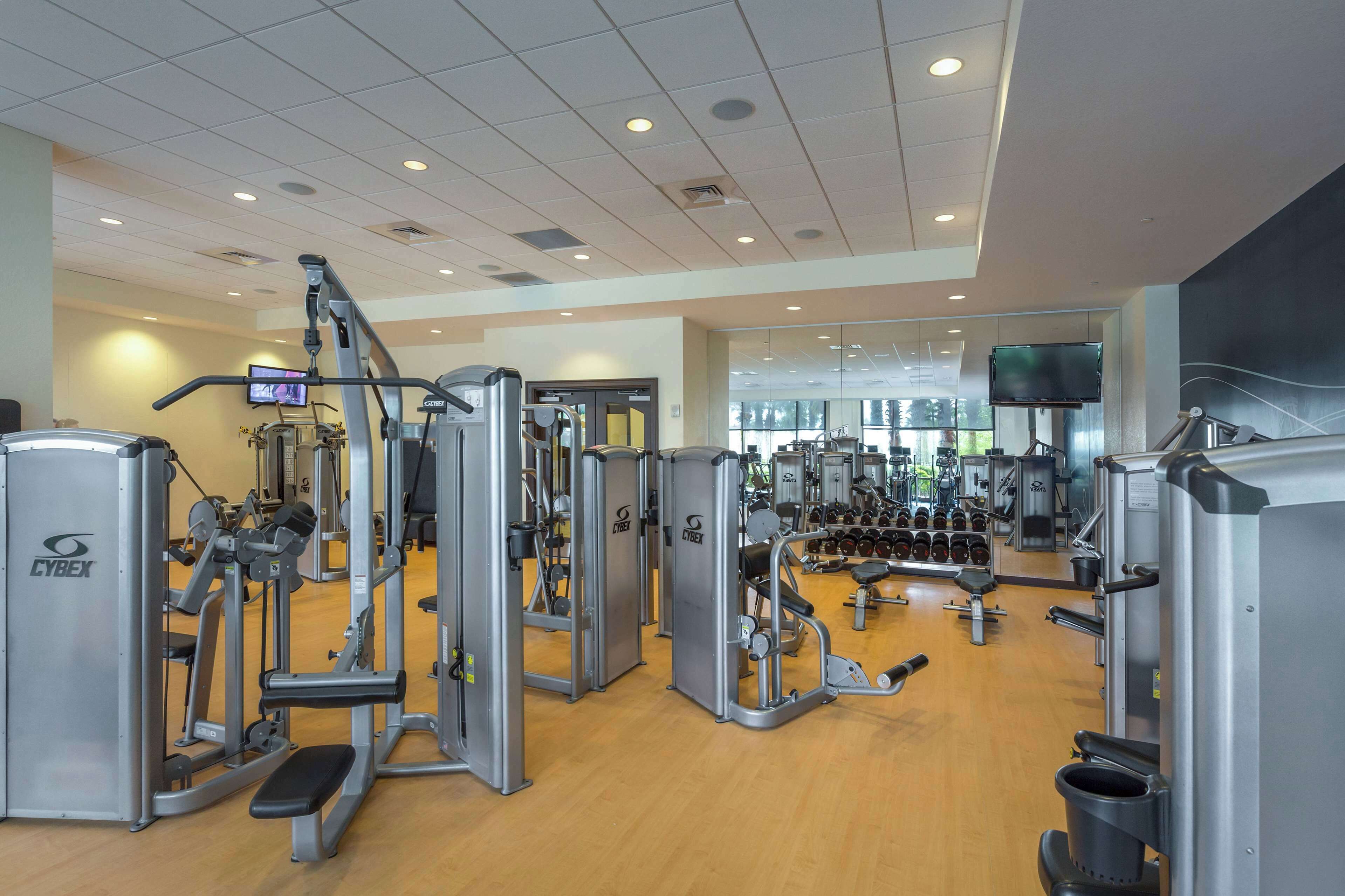 Un gimnasio con diferentes máquinas de ejercicio, un televisor y un espejo.