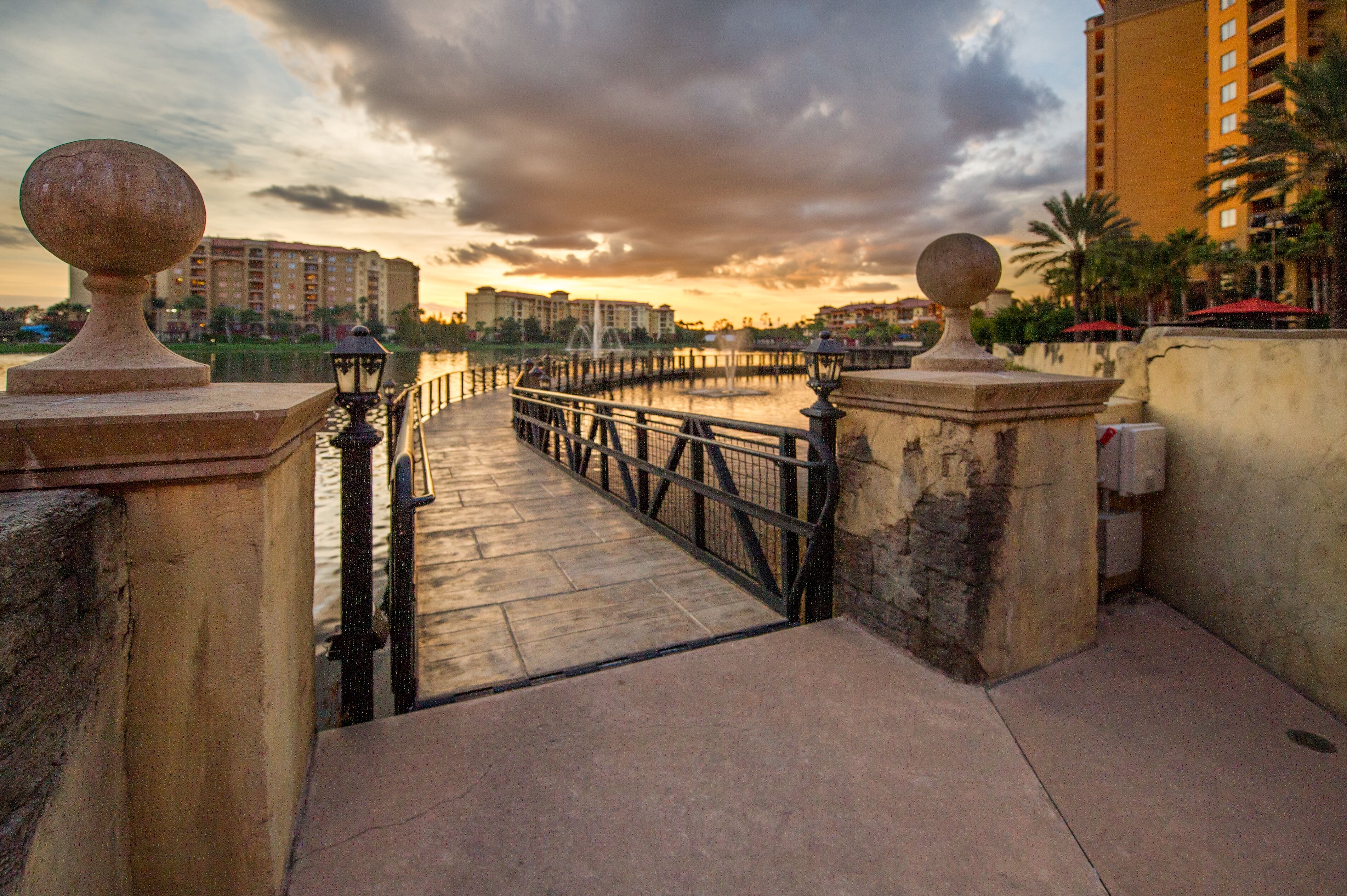 A waterfront promenade with a stone balustrade, a bridge, and a cityscape in the background.