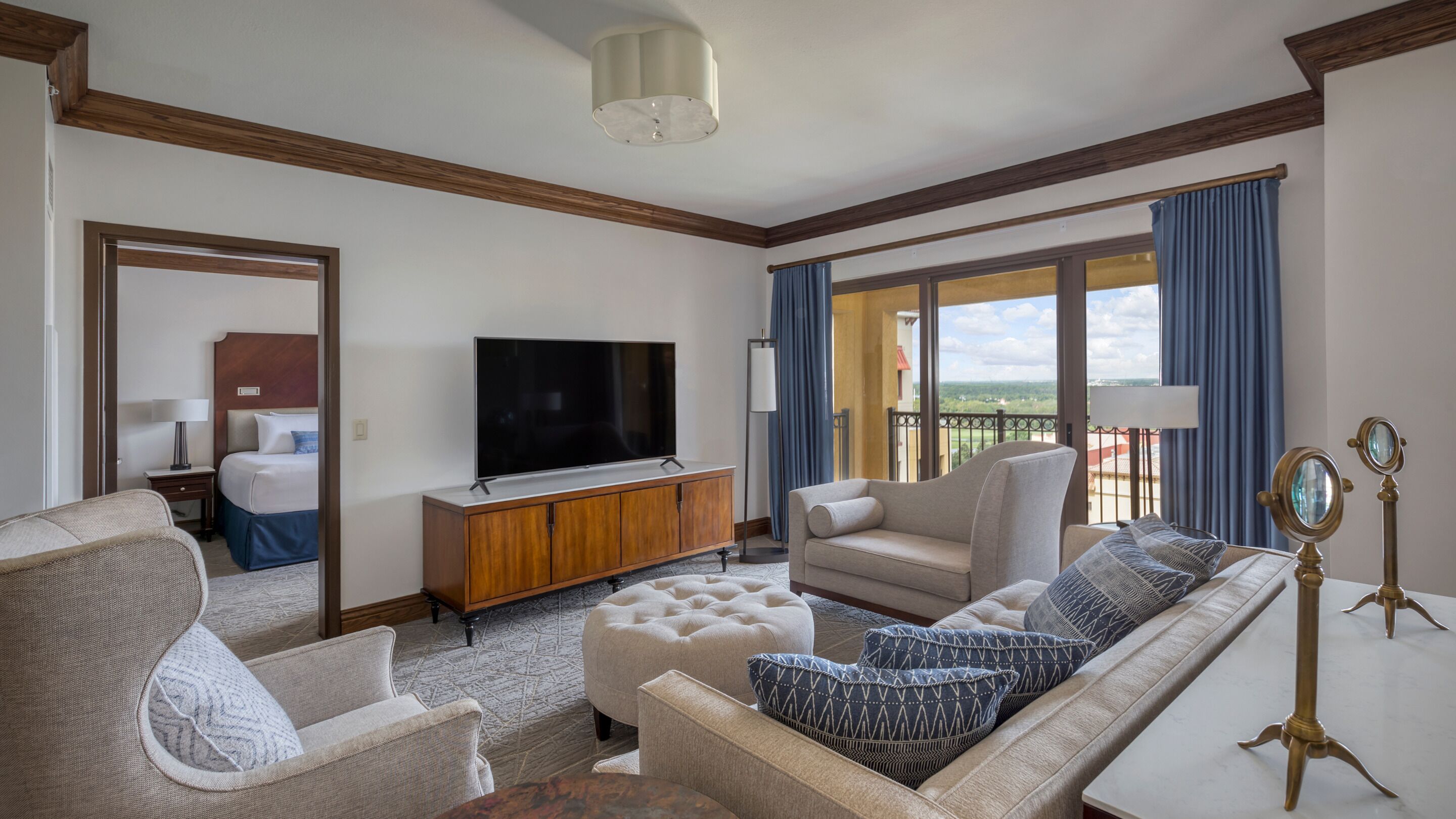 A modern hotel room with a large flat-screen TV, a sofa, a loveseat, and a dining table.