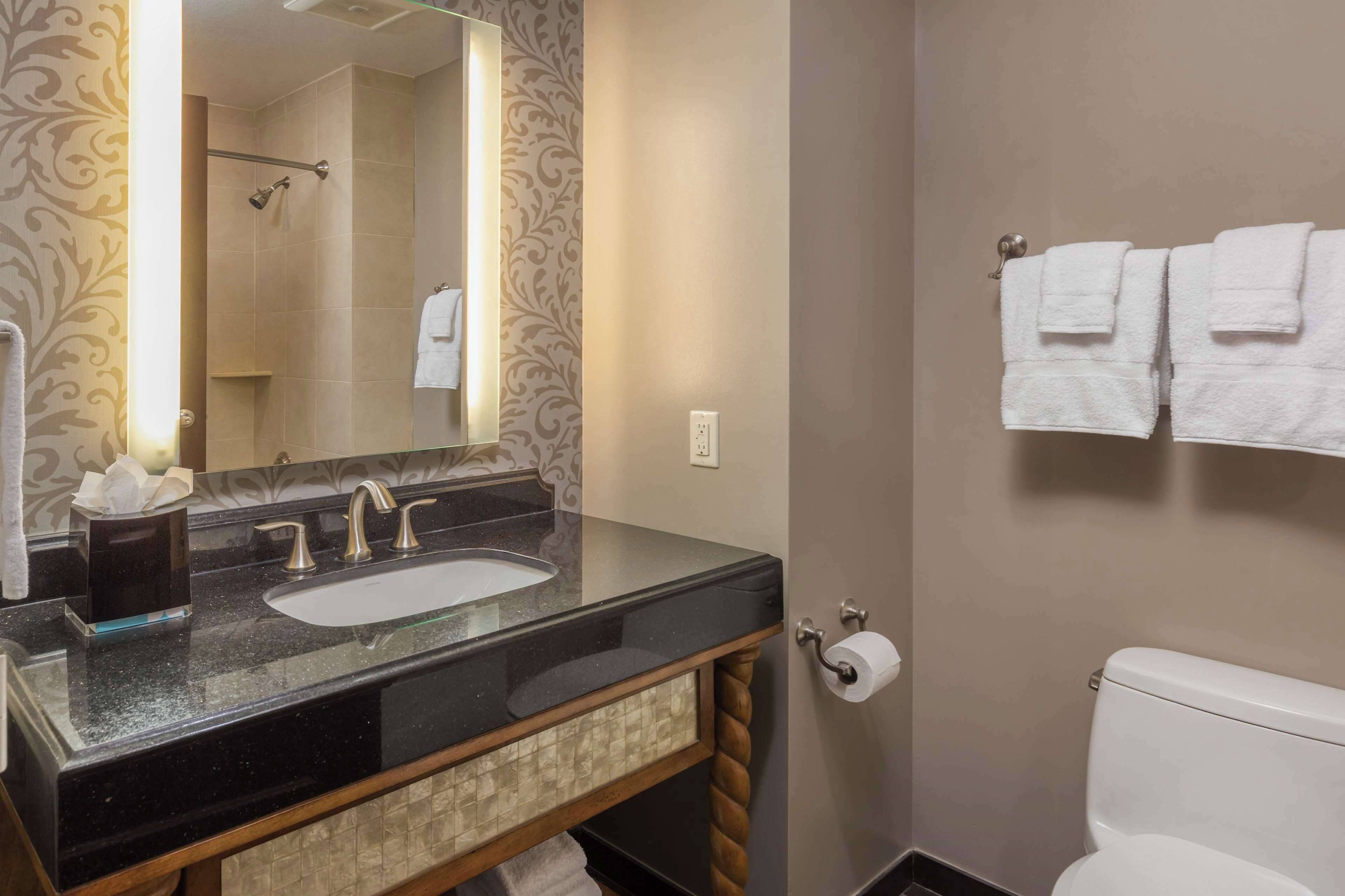 Une salle de bain avec un lavabo en granit noir, un miroir, un porte-serviettes avec des serviettes blanches et des toilettes.