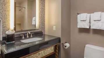 Een badkamer met een zwart granieten wastafel, een spiegel, een handdoekhouder met witte handdoeken en een toilet.