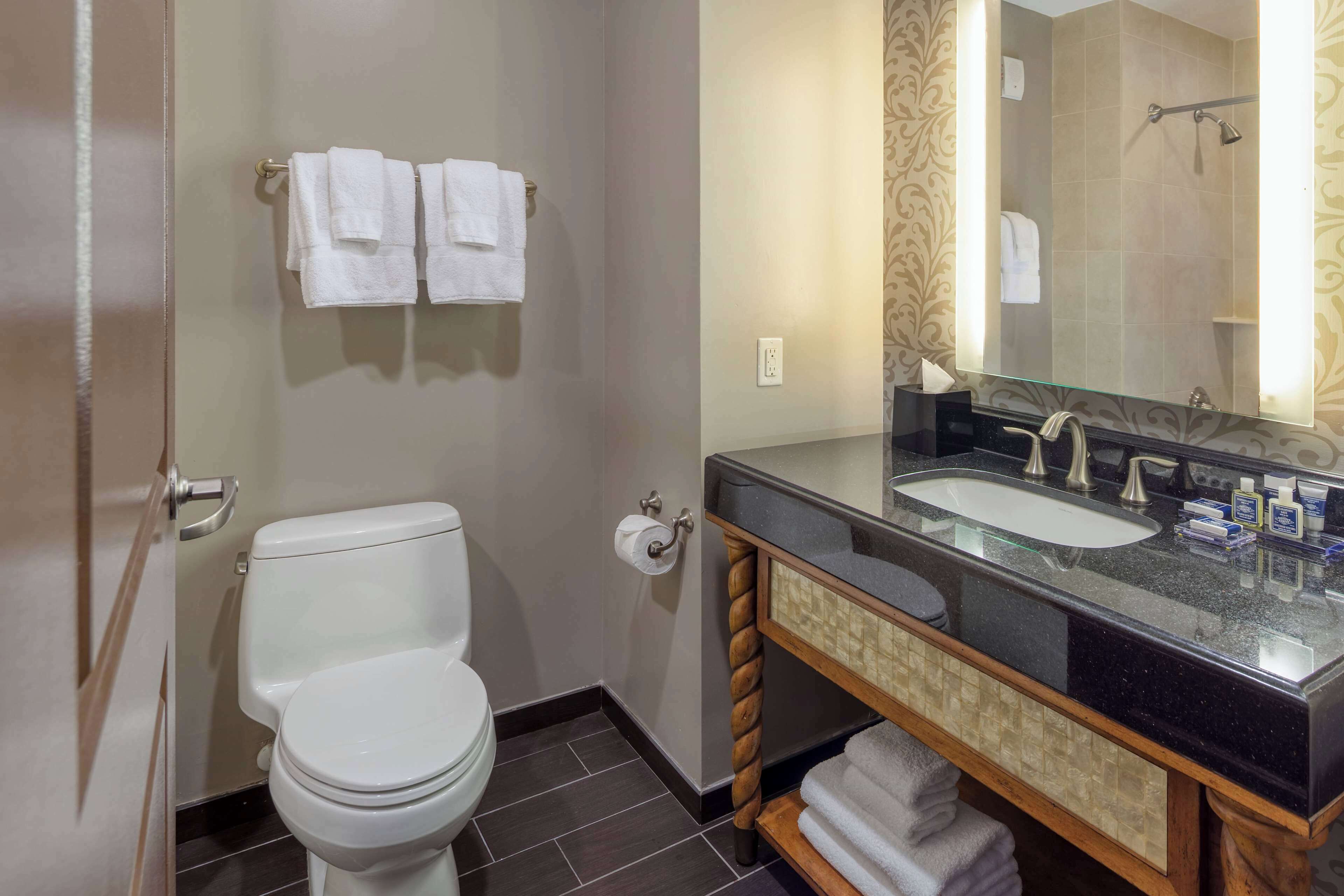 Un baño moderno con inodoro blanco, lavamanos con espejo y zona de ducha.