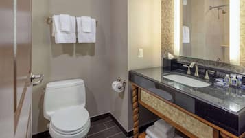 Un baño moderno con inodoro blanco, lavamanos con espejo y zona de ducha.
