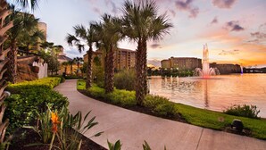 A pathway leading to a body of water with a fountain, surrounded by palm trees and a building with multiple floors. - Wyndham Grand Orlando Resort Bonnet Creek (Orlando)