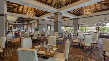 Un comedor amplio con varias mesas dispuestas para los huéspedes, elegantes candelabros y vistas al exterior.