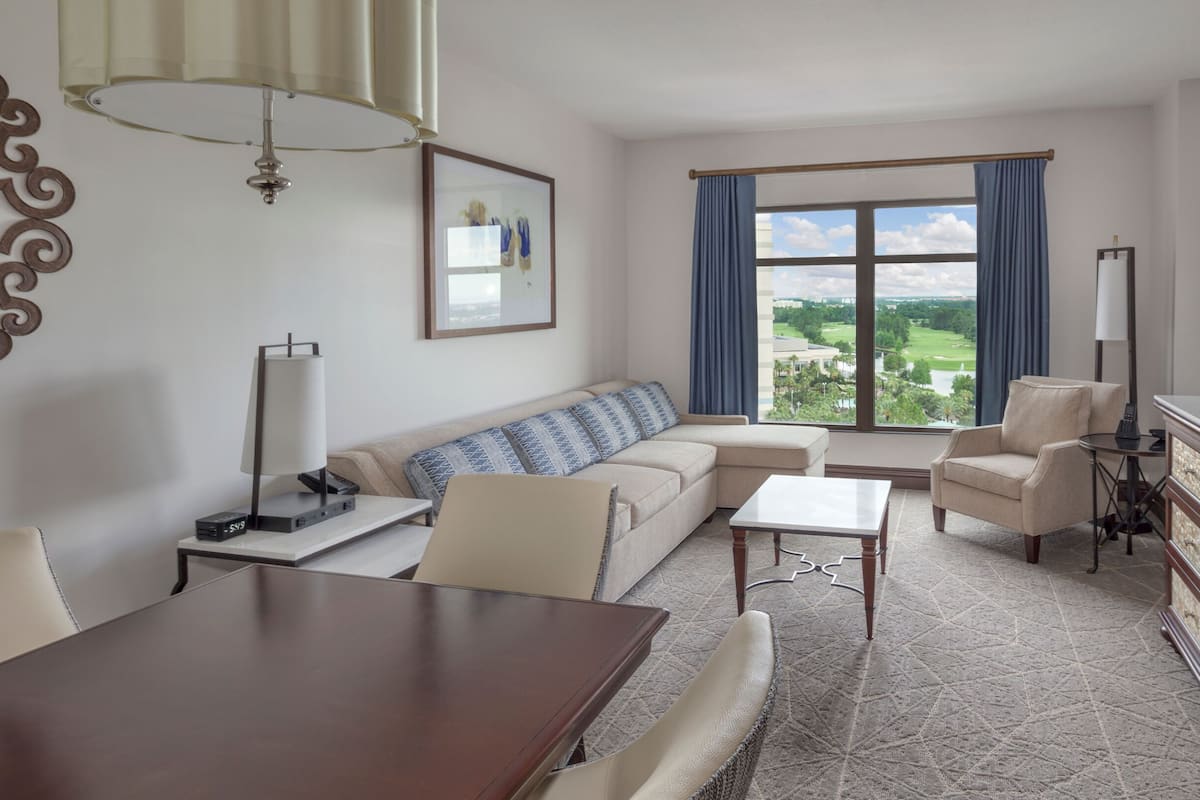 Een moderne woonkamer met een bank, fauteuils, een eettafel en uitzicht op een golfbaan.