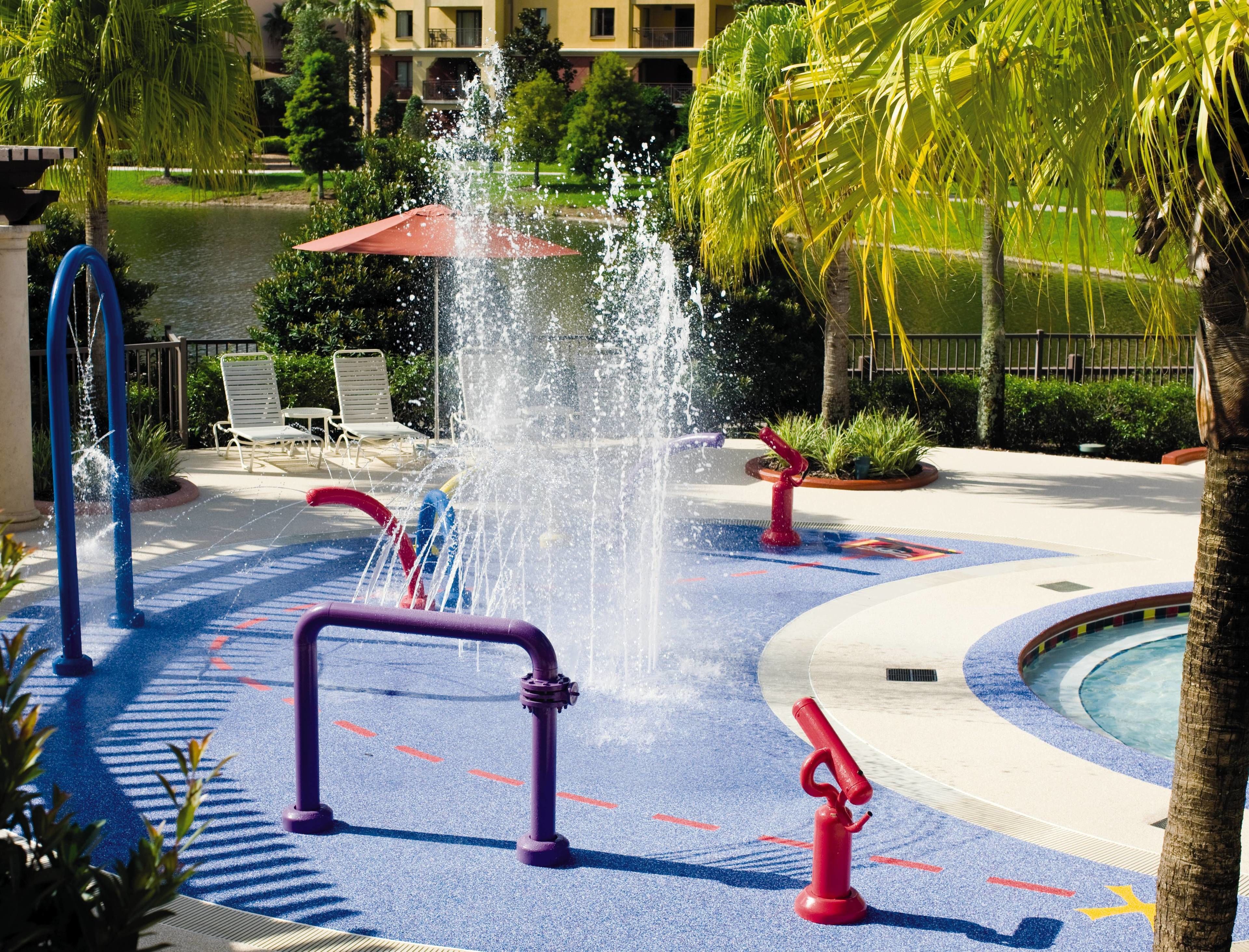 A water play area with a pool, a red umbrella, and a palm tree.