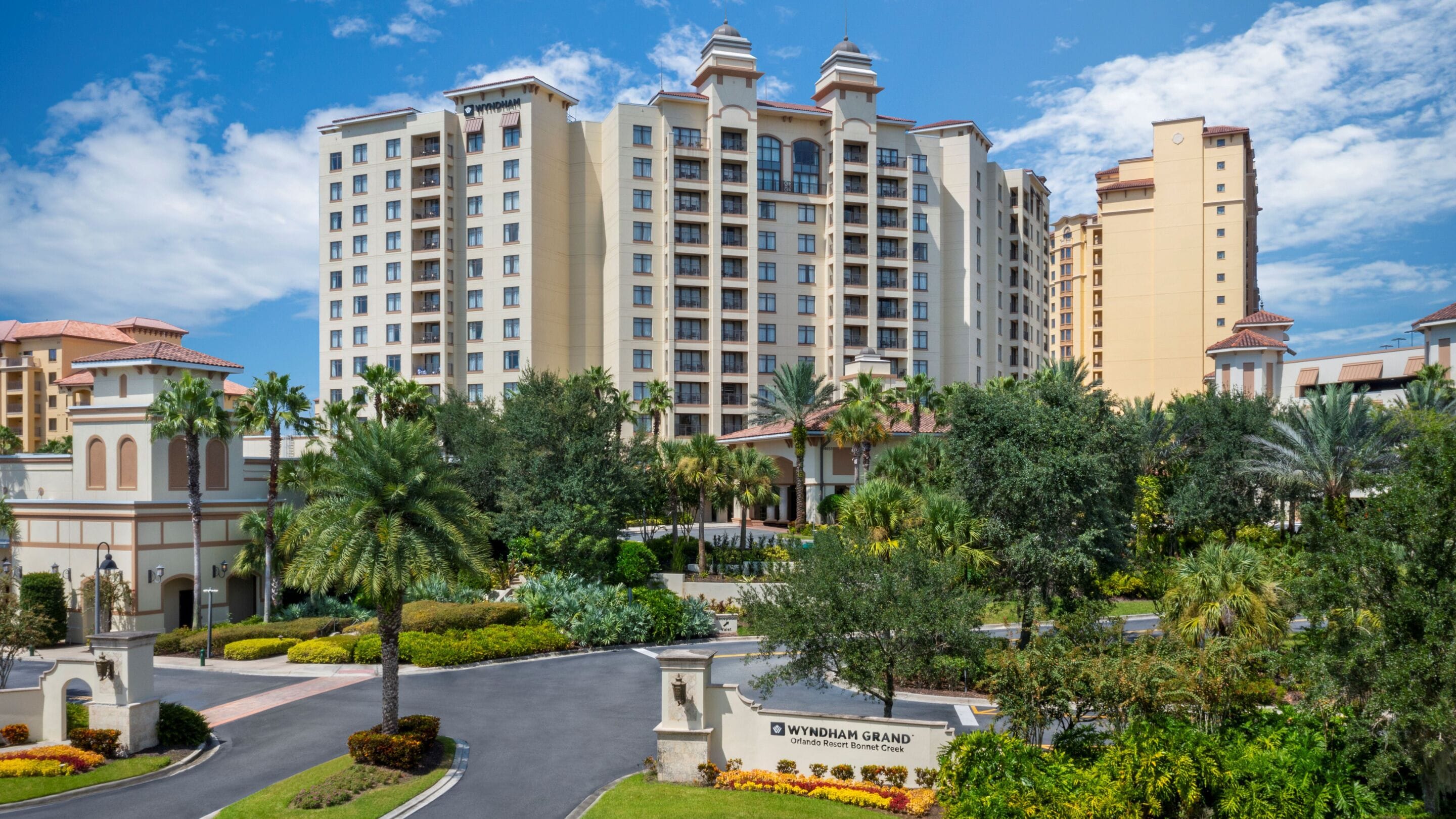 A multi-story hotel with a central courtyard, palm trees, and a clear sky.