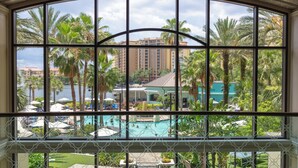 A view through a large window of a resort with a pool, palm trees, and a building in the background. - Wyndham Grand Orlando Resort Bonnet Creek (Orlando)