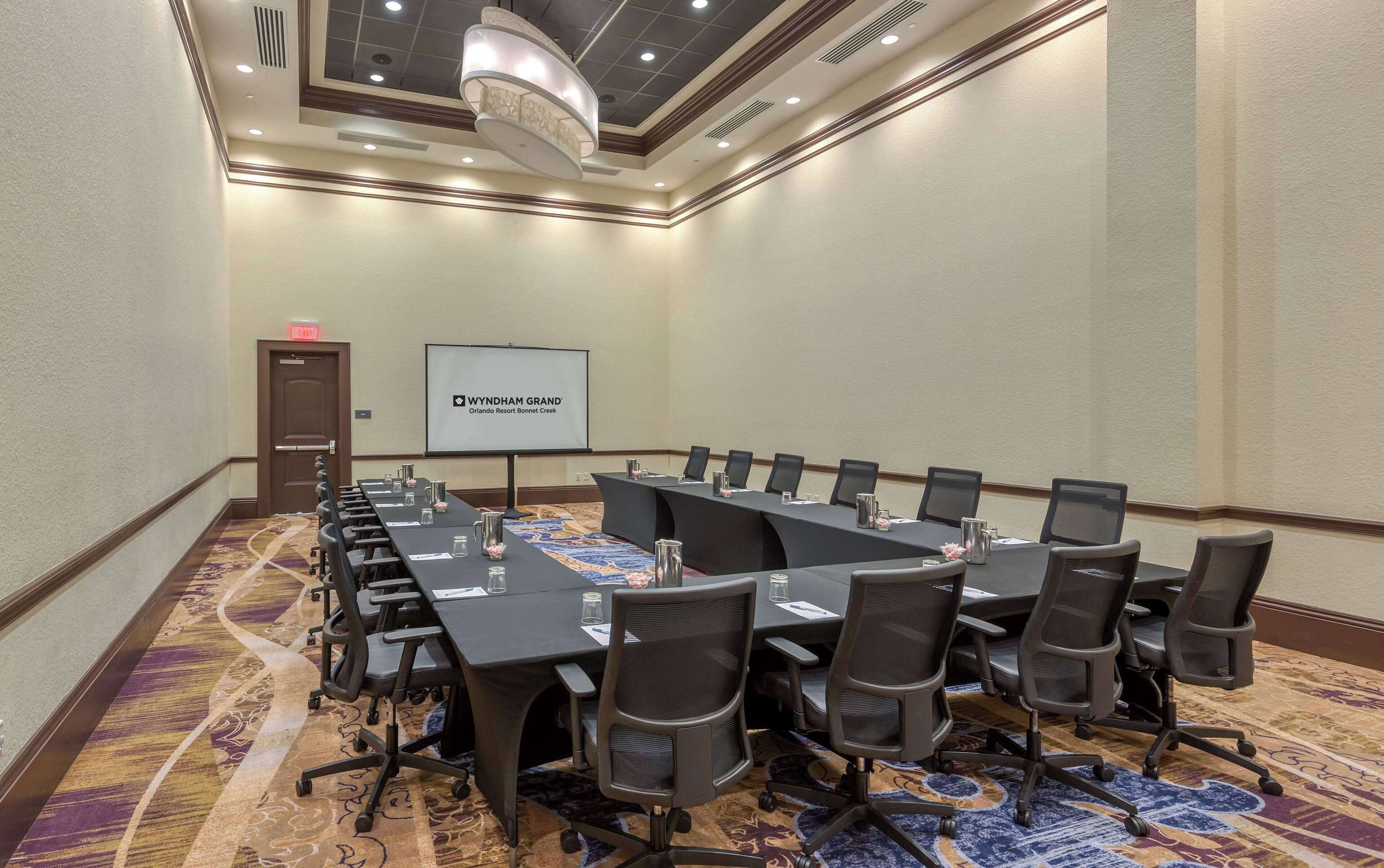 A conference room with a long table, chairs, a projector screen, and a carpeted floor.