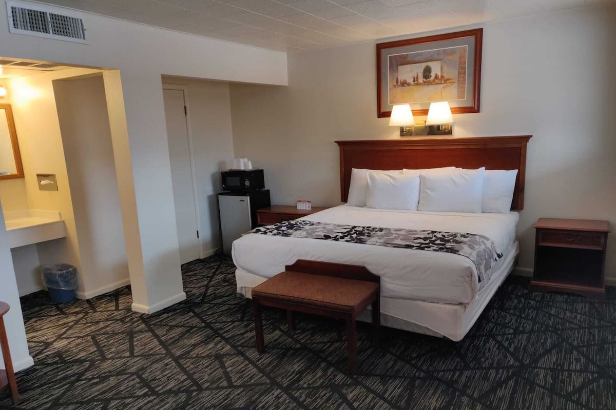 A hotel room with a large bed, a desk with a computer, a small refrigerator, and a trash can.