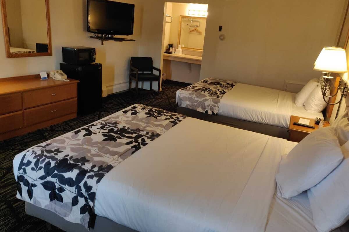 A hotel room with two beds, a TV, a desk with a telephone, and a bathroom visible through an open door.