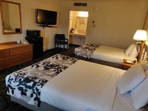 Quarto de hotel com duas camas, televisão, secretária com telefone e banheiro visível por uma porta aberta.