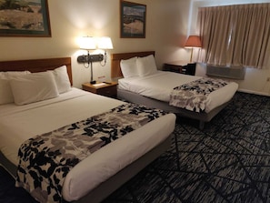 A hotel room with two beds, a nightstand, a lamp, and a window with curtains.