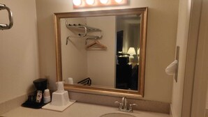 Een hotelbadkamer met een grote spiegel, een wastafel en een opbergmeubel met toiletartikelen.