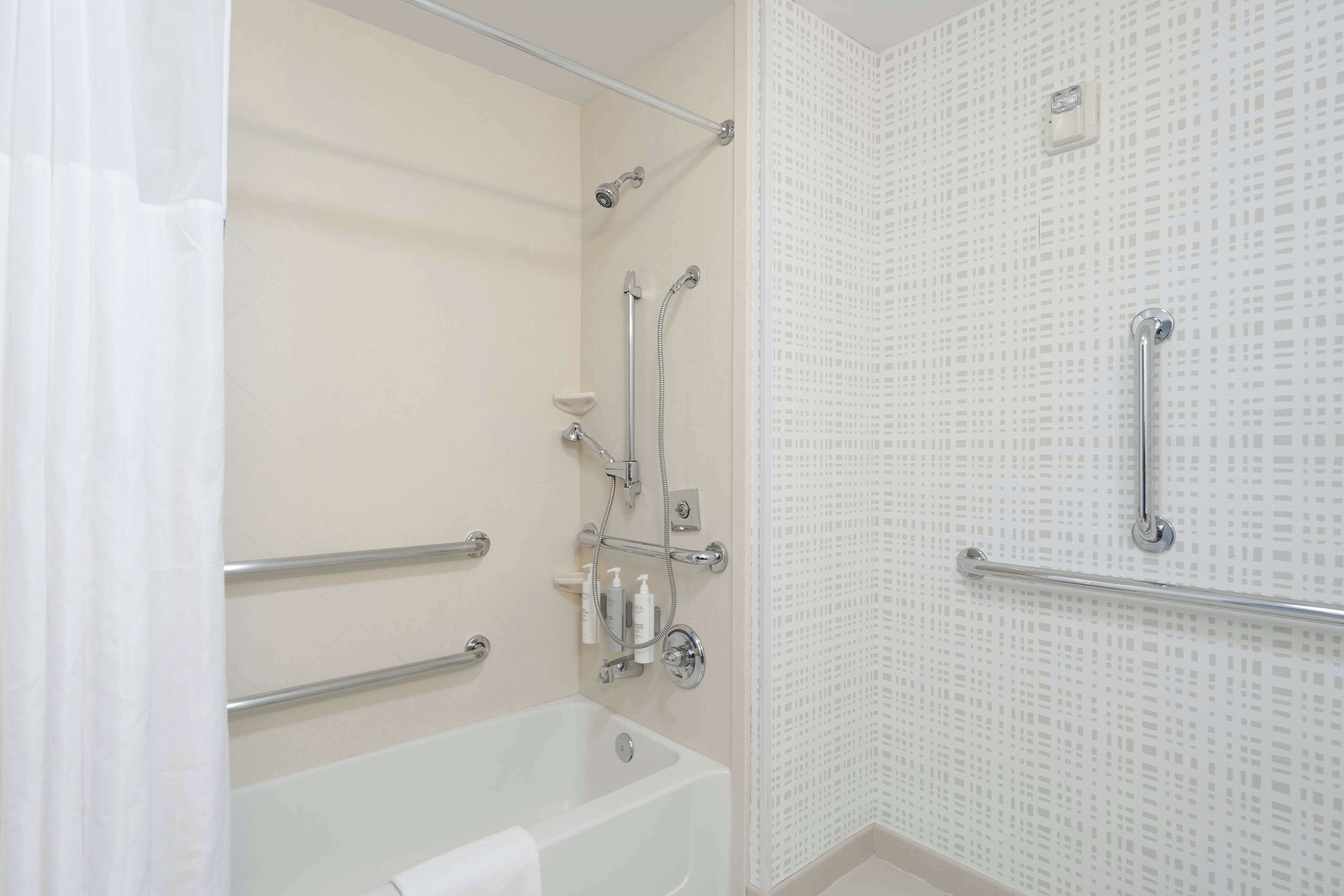 A modern bathroom with a bathtub, shower, and grab bars.