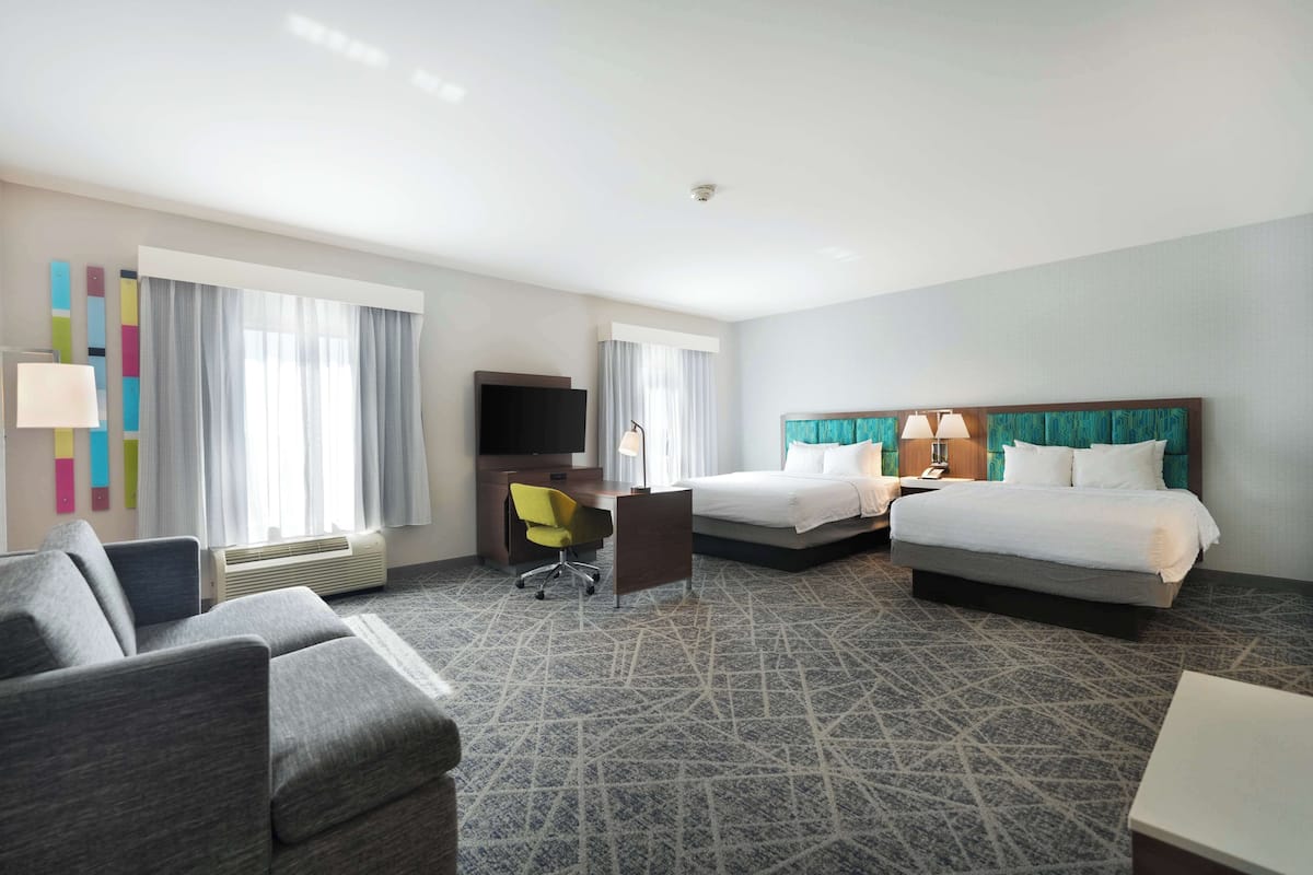A hotel room with two beds, a desk, a chair, a TV, and a window with curtains.