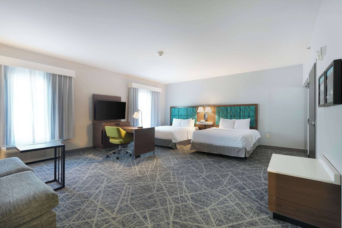A hotel room with two beds, a desk, a chair, a TV, and a minibar.