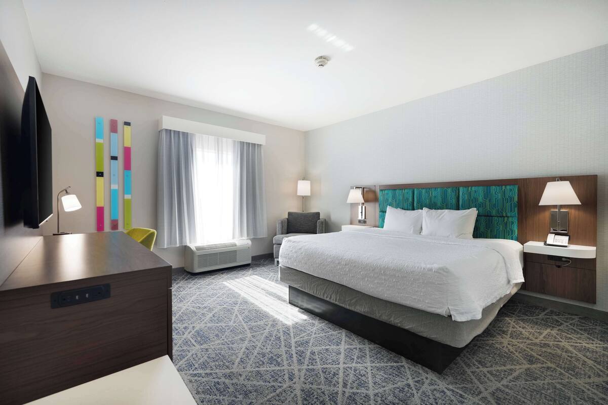 A hotel room with a large bed, a desk, a TV, and a window with curtains.