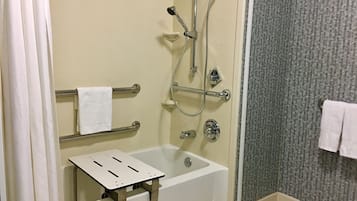 Un baño con ducha a nivel, barras de apoyo, una bañera blanca y un perchero para toallas.