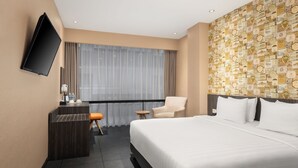 Habitación de hotel con una cama grande, un escritorio con silla, televisor y ventana con cortinas.