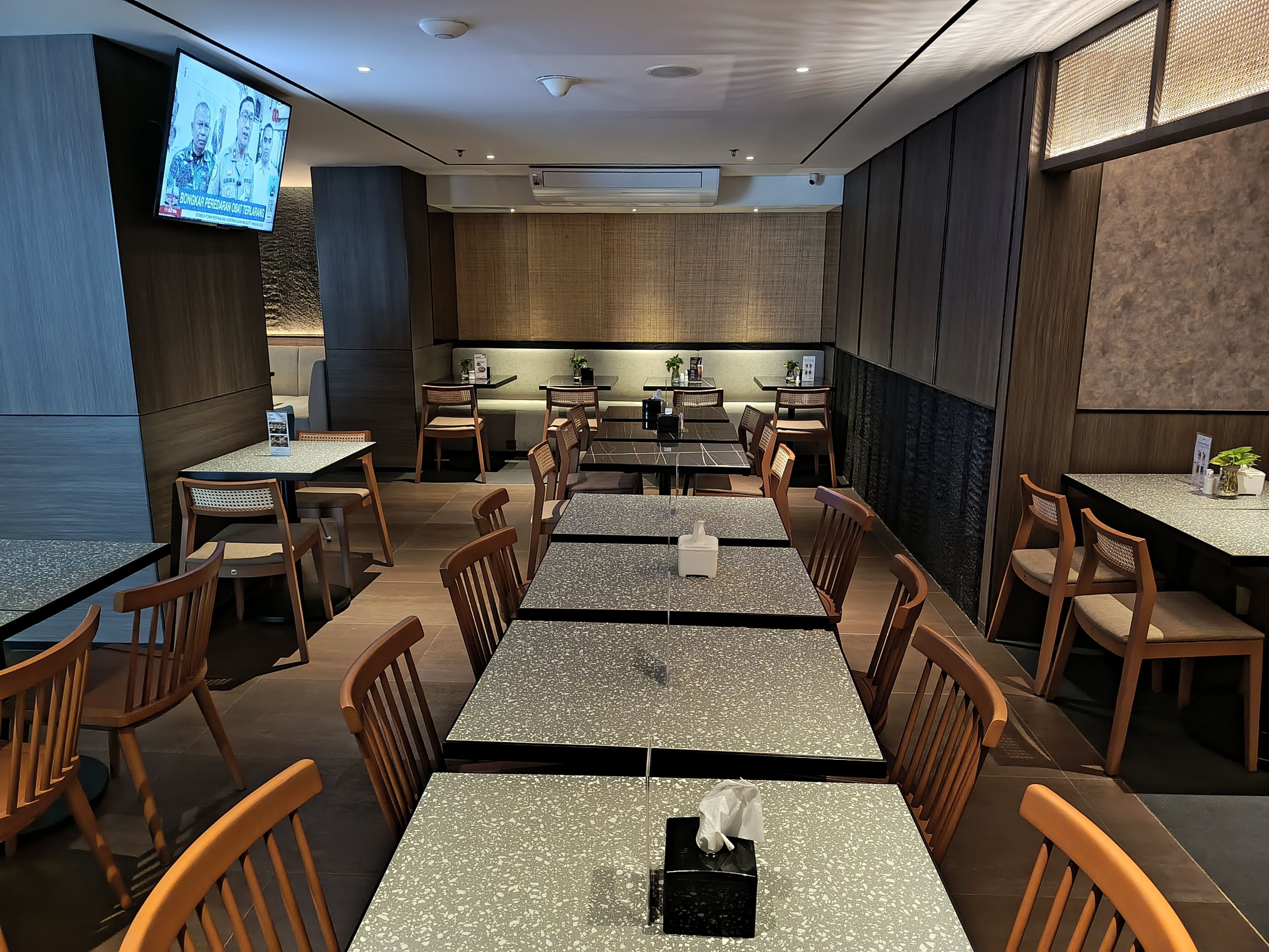 A restaurant with multiple tables and chairs, a television screen, and a modern interior design.