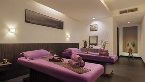 Un cuarto de spa con dos camillas de masaje, cada una con una toalla y una bandeja de detalles.
