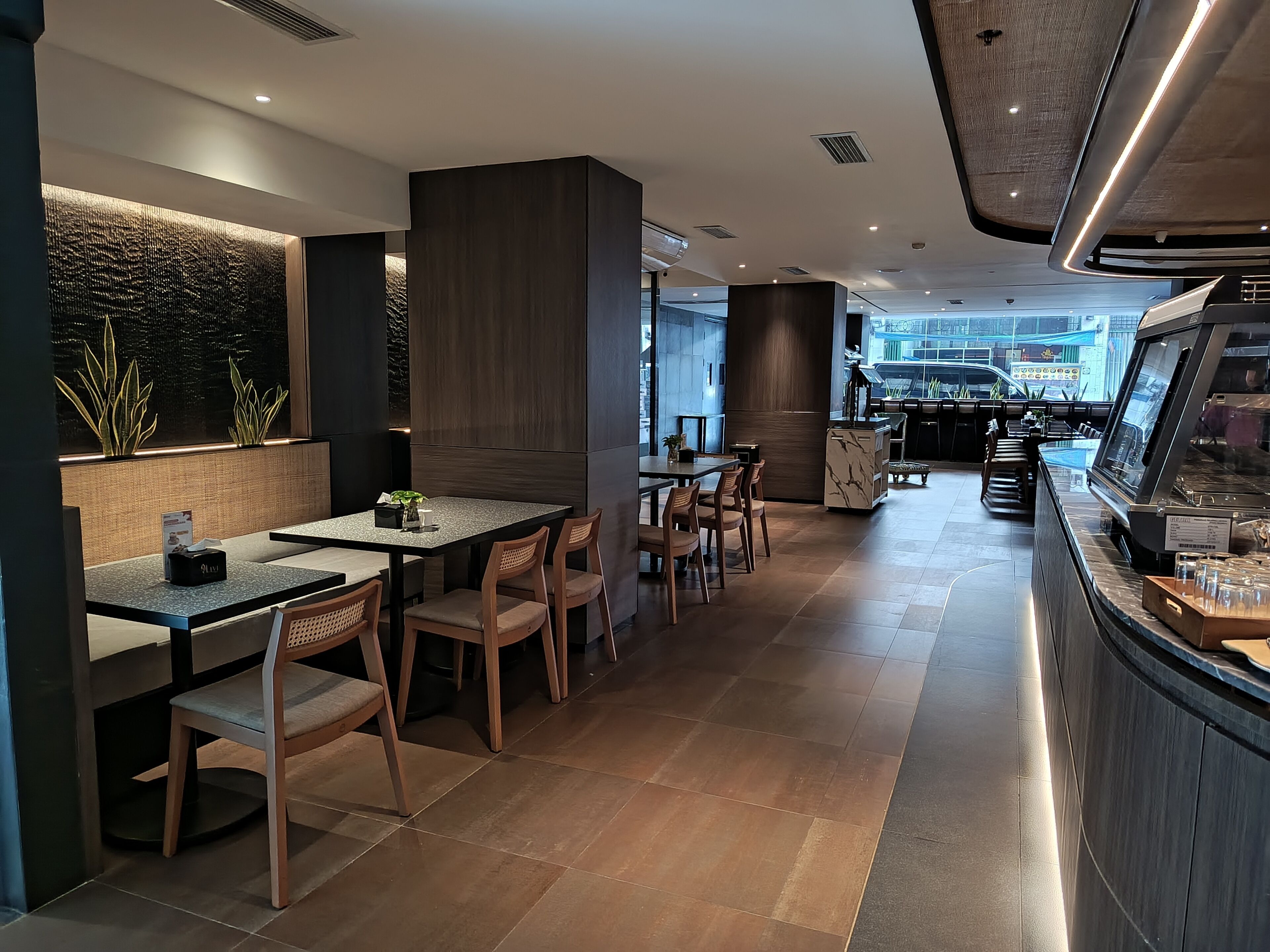 Een modern restaurantinterieur met een lange toonbank, houten stoelen en uitzicht op de straat.