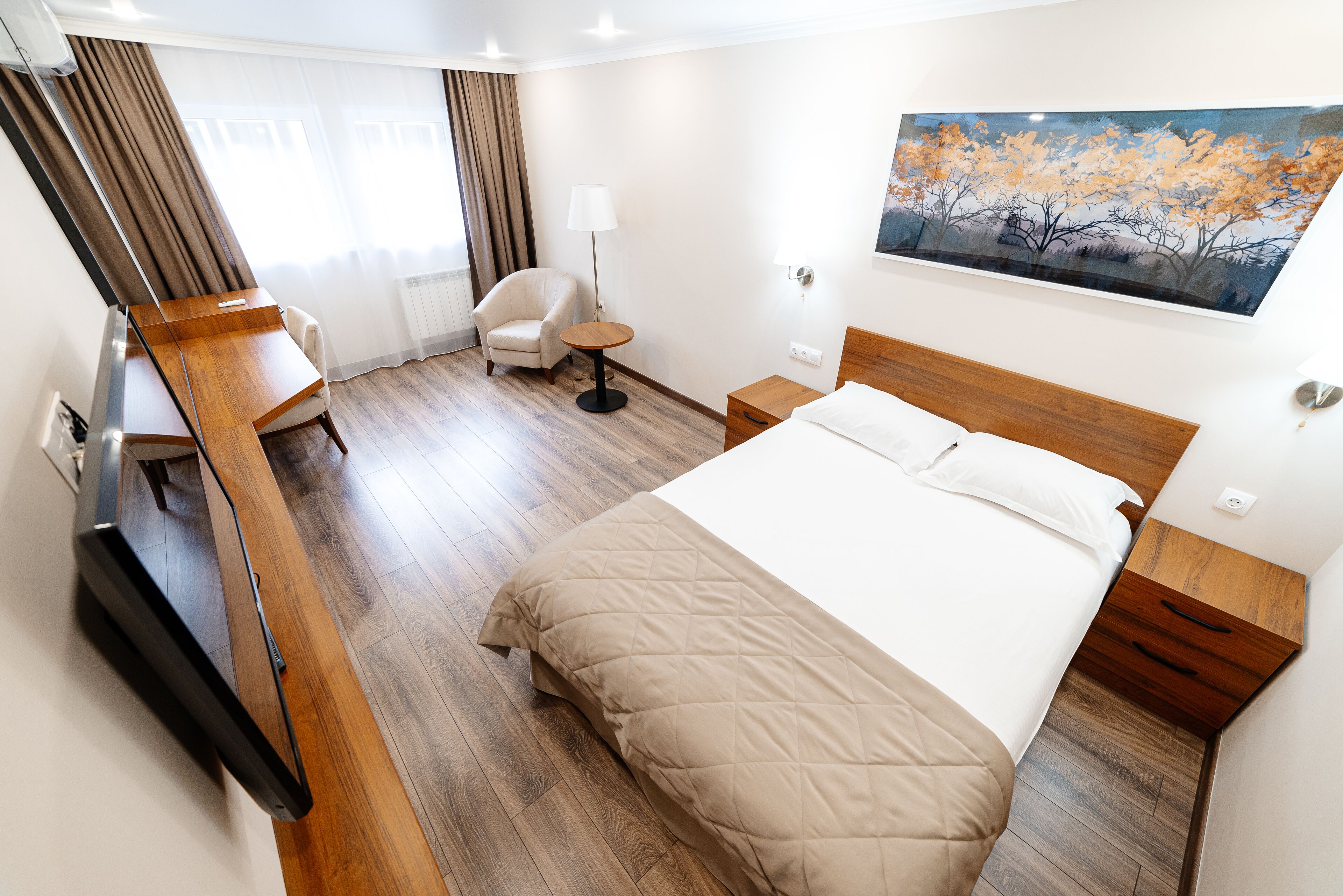 Habitación de hotel con cama, escritorio, silla, lámpara y un cuadro en la pared.
