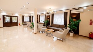 A spacious lobby with a modern design, featuring a seating area with sofas and armchairs, a coffee table, and potted plants. - Chagala Uralsk Hotel (Uralsk)