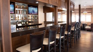 A bar area with wooden cabinets, a TV screen, and bar stools. - Chagala Uralsk Hotel (Uralsk)