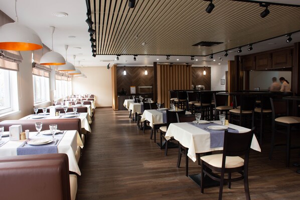 A restaurant with multiple dining tables, chairs, and pendant lighting.