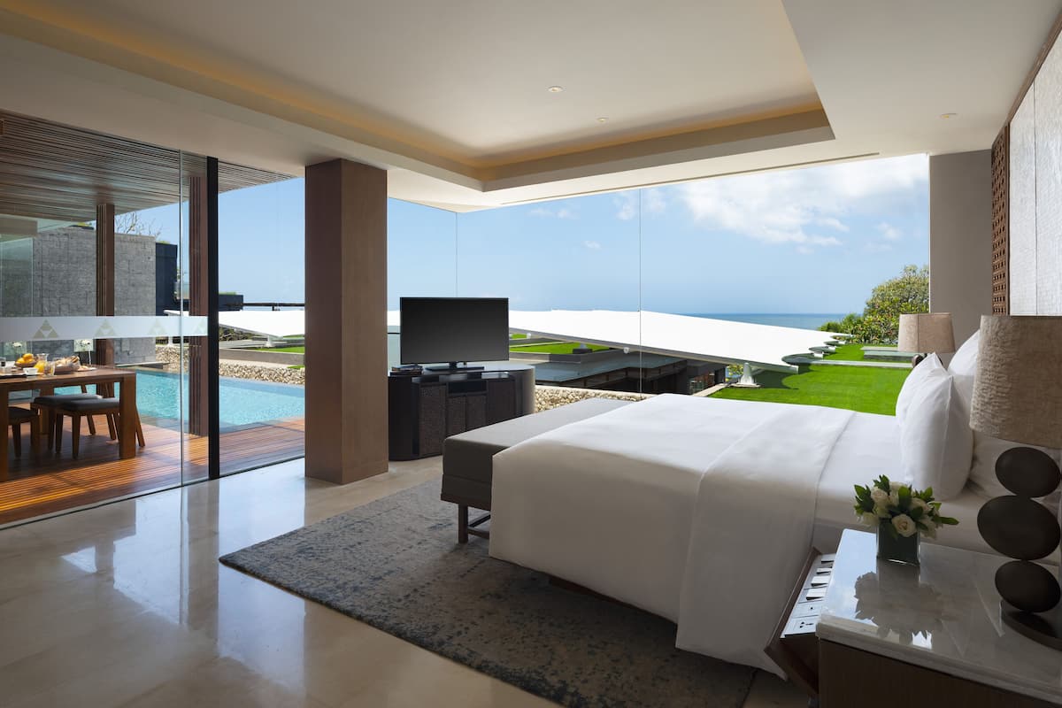 A modern bedroom with a large bed, a TV, and a view of the ocean.