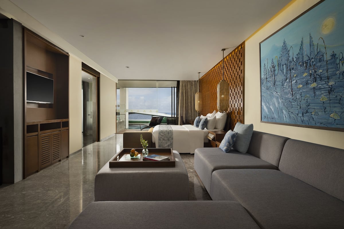 A modern hotel room with a large window, a sofa, a coffee table, and a painting on the wall.