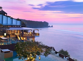 A resort with a pool, outdoor seating, and a view of the sea at sunset.