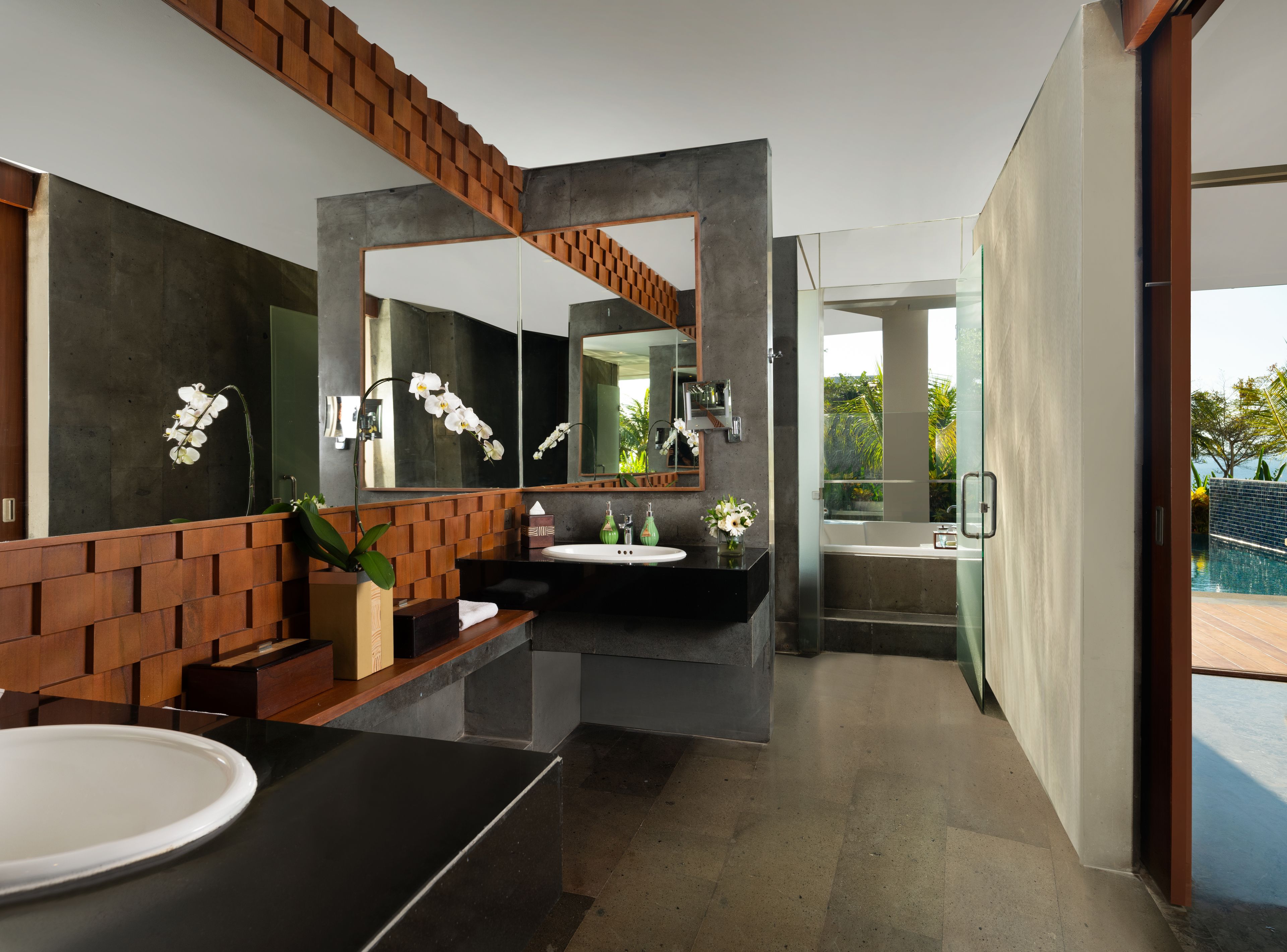 A modern bathroom with a large mirror, a wooden bench, and a view of a pool.