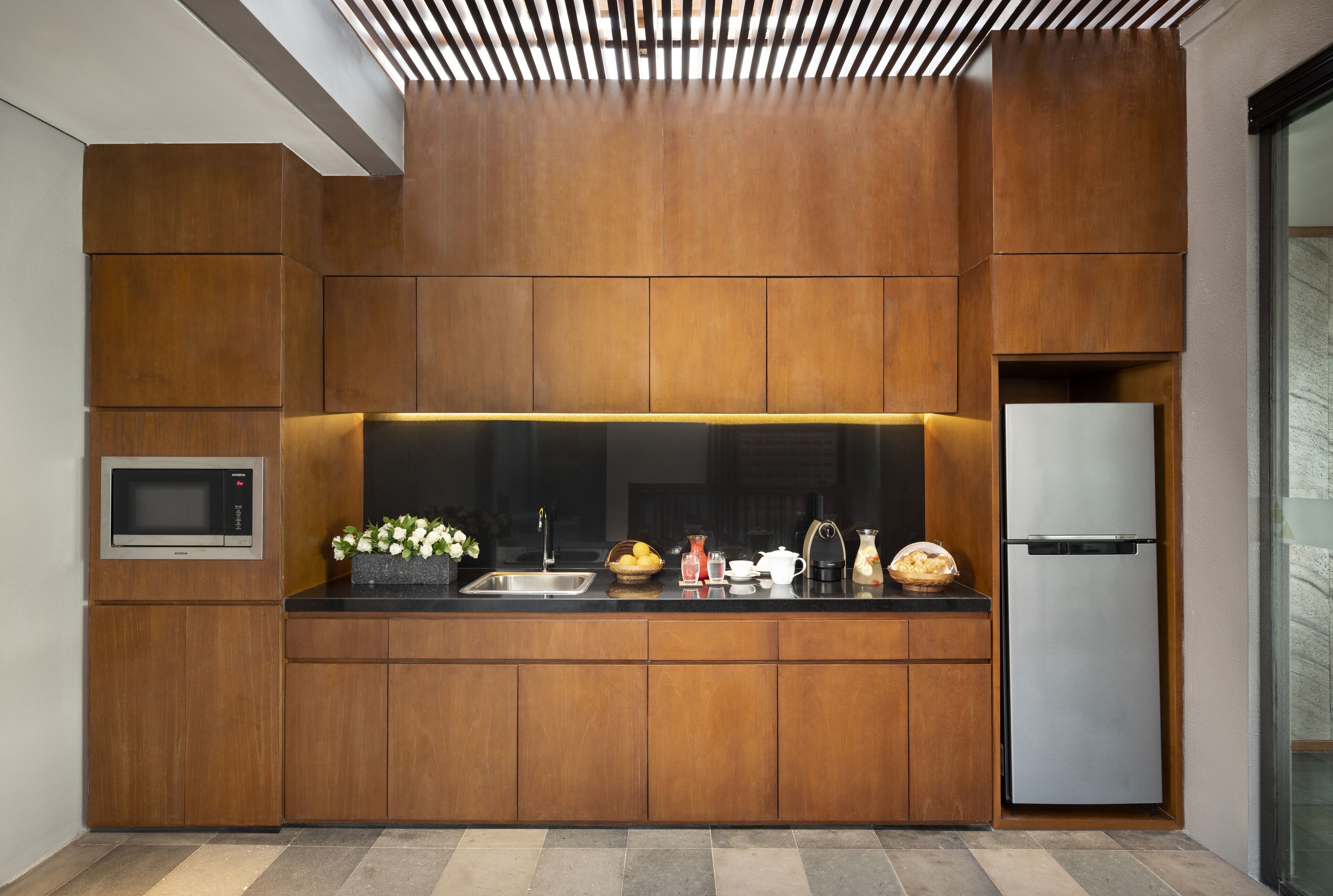 Una cocina moderna con armarios de madera, microondas integrado y refrigerador de acero inoxidable.