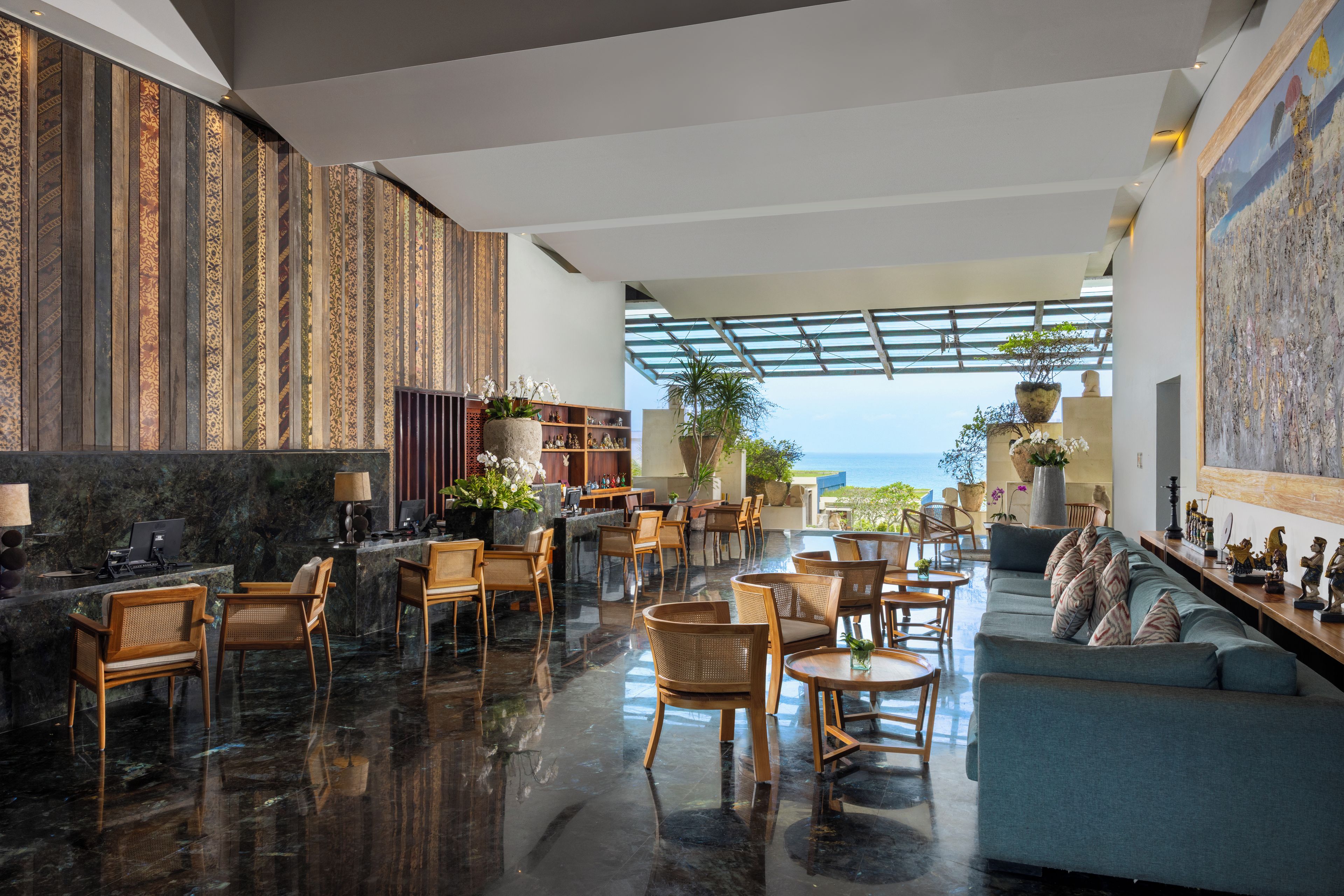 A modern hotel lobby with a reception desk, seating area, and a view of the ocean.