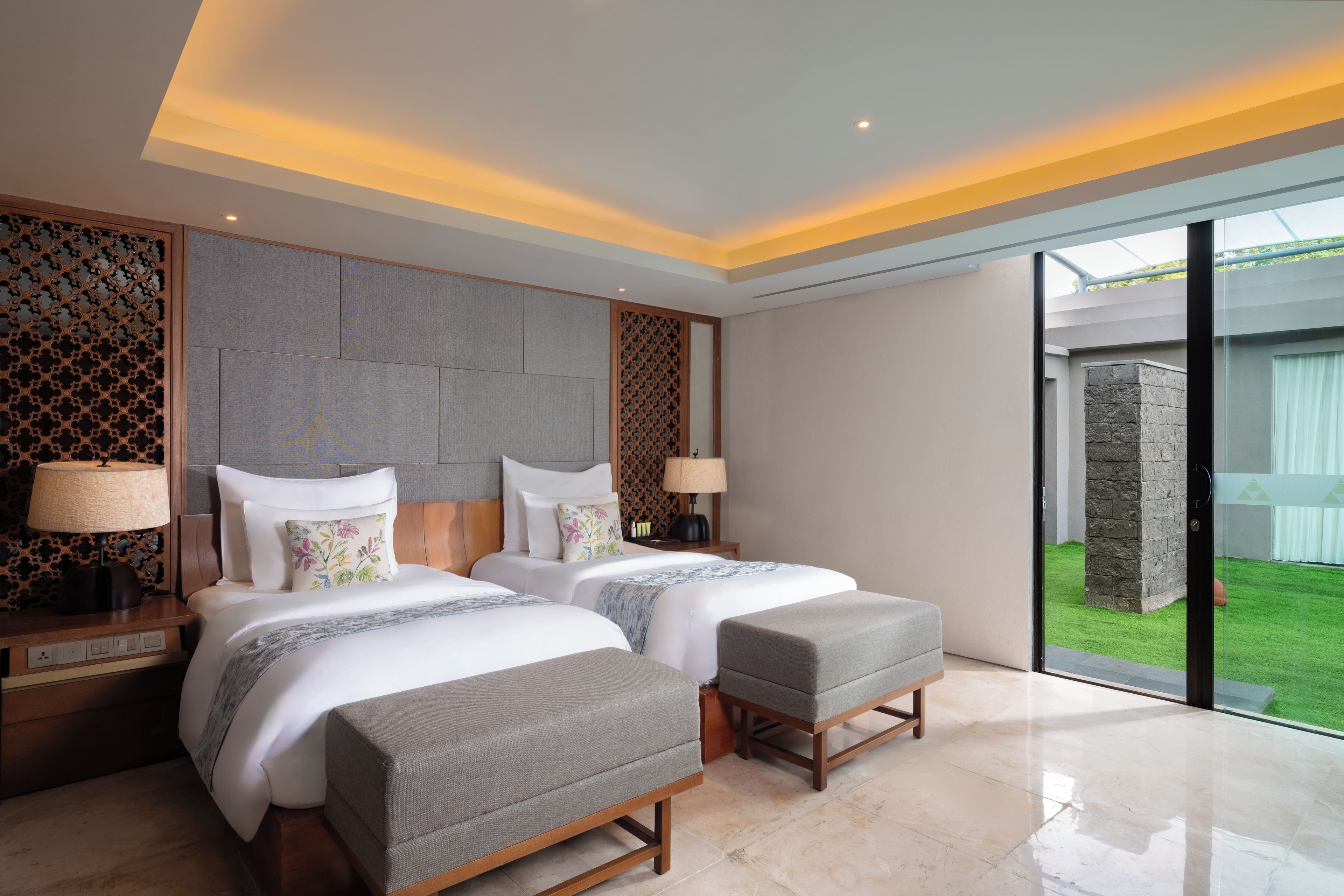 Une chambre d’hôtel moderne avec deux lits, une grande fenêtre et une vue sur un jardin.